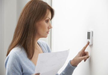 A woman adjusting the thermostat in a home while holding an energy bill.