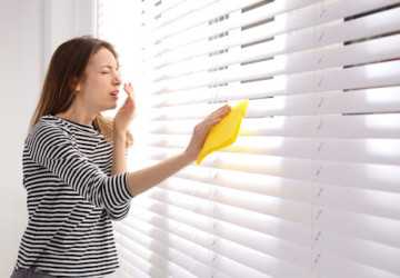 A woman cleaning window blinds with a cloth. She looks like she is about to sneeze.