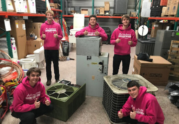 5 Arllinghaus team members giving a thumbs up while standing around air conditioning and furnace units in their warehouse.