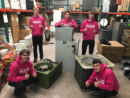 5 Arllinghaus team members giving a thumbs up while standing around air conditioning and furnace units in their warehouse.