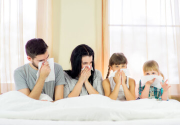 A family of four sitting up in a bed and blowing their noses due to poor IAQ.