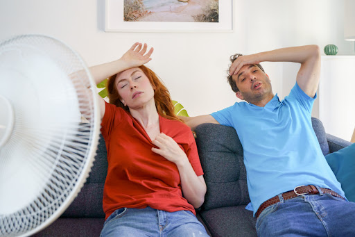 Couple sitting on the couch with a fan blowing on them due to high humidity in the home.