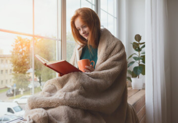 A woman sitting on a windowsill and reading a book.