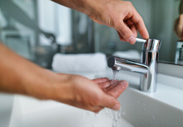 A person putting their hand under a faucet to feel the temperature of the water.