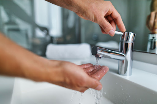 A person putting their hand under a faucet to feel the temperature of the water.