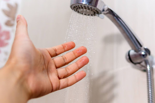 A hand testing the temperature of shower water.