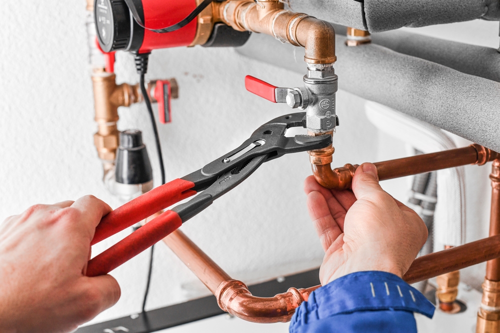 A person using pliers to tighten a valve on copper pipes in a plumbing system.