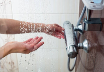 A person testing the water temperature in a shower.