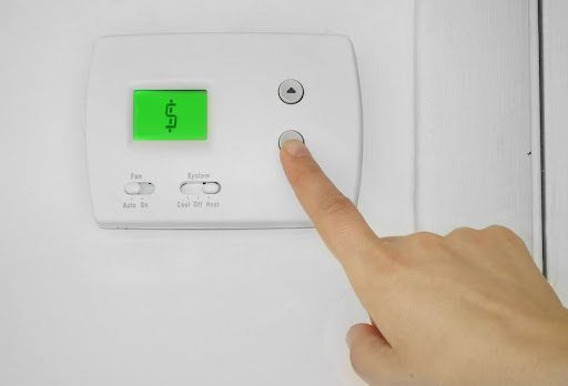 A close-up of a hand adjusting the temperature on a thermostat; the thermostat is displaying a money sign on the screen.