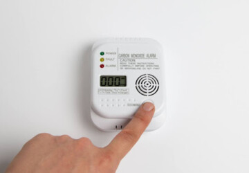 A finger pressing a button to test a carbon monoxide alarm that has been installed on a white wall.