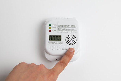 A finger pressing a button to test a carbon monoxide alarm that has been installed on a white wall.