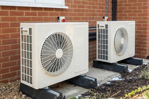 Two heat pumps installed outside on concrete slabs.