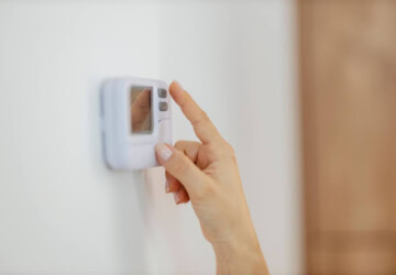 A close-up of a woman's hand adjusting a thermostat in a home.