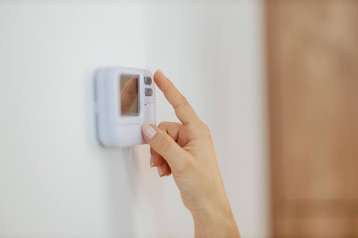 A close-up of a woman's hand adjusting a thermostat in a home.