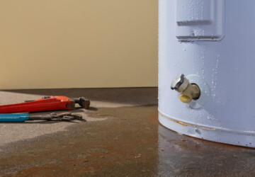 A leaking water heater tank with tools on the ground beside it.